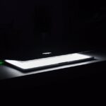 A dramatic, low-light image of a slightly open laptop with glowing keys on a dark desk.