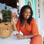 Home Stylish woman in orange outfit enjoying ice cream at a charming outdoor cafe, exuding summer vibes.